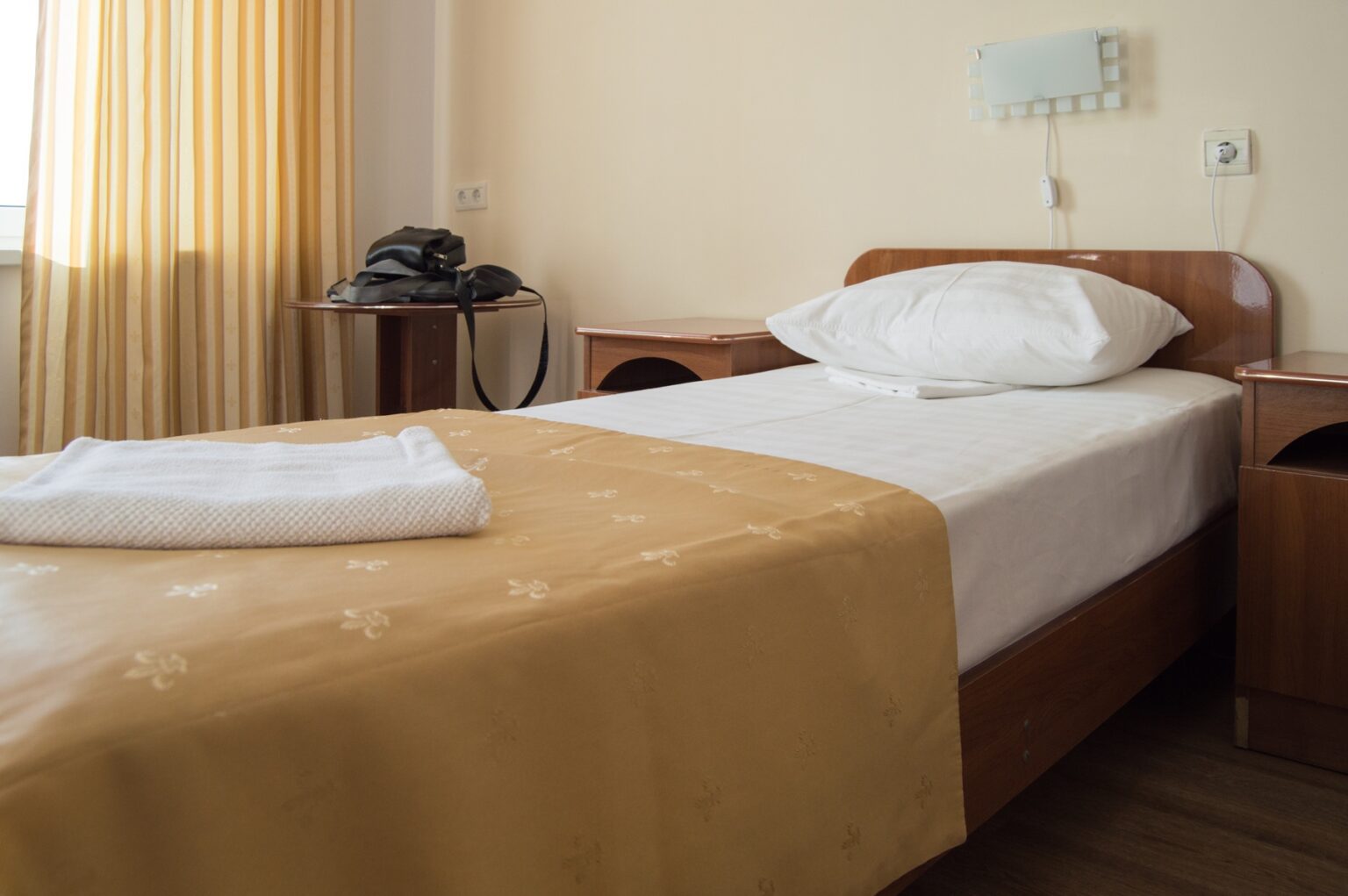 Hotel single Room with a bed, an armchair and a table with men's black bags.